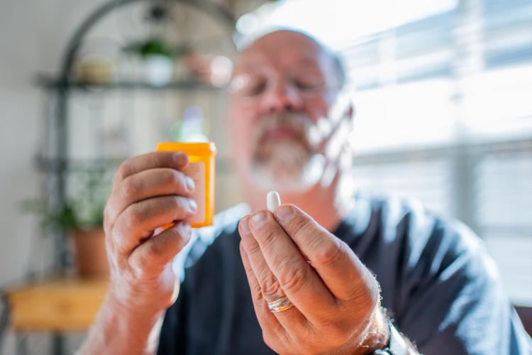 Mature man holding pill bottle in one hand and one pill in another hand.
