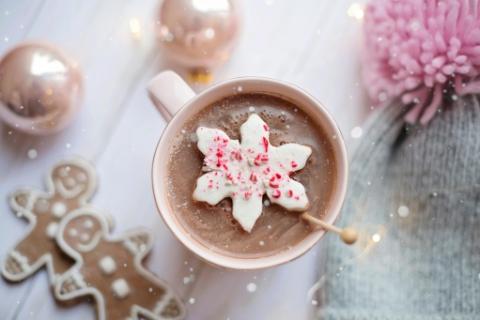 View of cup of hot cocoa from above with a peppermint biscuit on top and gingerbread men on counter next to it