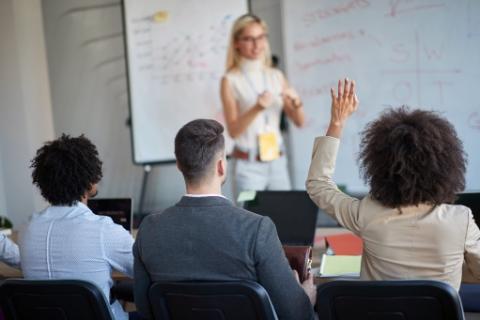 Three people seated in front of blurred-out workshop presenter with one person having their hand raised