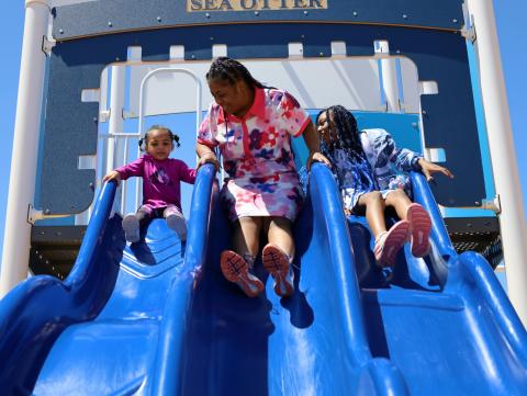 mother with two children, girls, sliding down three blue slides in playground